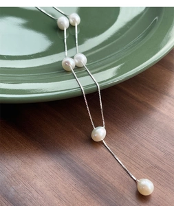 Detail of S925 silver necklace with six lustrous white pearls on a green ceramic plate