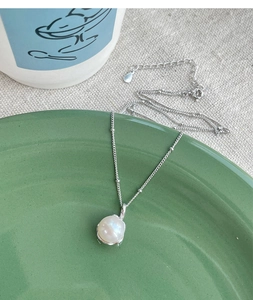 Detail of single freshwater pearl pendant on a silver-tone beaded chain over green ceramic
