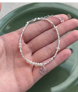 Macro detail of S925 silver beaded bracelet featuring pearl accents and Fu character charm