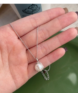 Close-up of a single freshwater pearl on a delicate silver chain held in hand