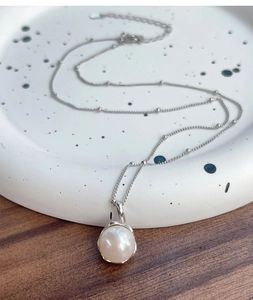 Close-up of elegant S925 silver necklace with single freshwater pearl on ceramic tray