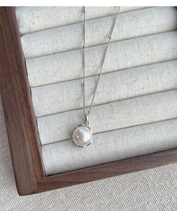 Close-up of a white freshwater pearl pendant with silver edging on a beaded chain necklace