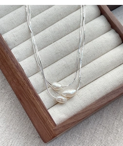 Dettaglio di una collana d'argento a strati con tre perle barocche su un vassoio di legno