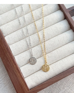 Close-up of gold and silver S925 sterling silver Fu character necklaces on linen padding