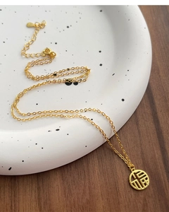 Detailed view of a gold S925 silver Fu pendant necklace on a ceramic plate background