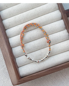 Macro detail of multi-color woven silk bracelet with silver bamboo-shaped metal beads