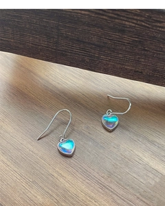 Detalle de pendientes de corazón en plata S925 con piedras de opalo irisadas en madera