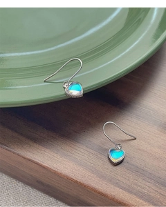 Primer plano de aretes de corazón en plata S925 con piedras iridiscentes en plato verde