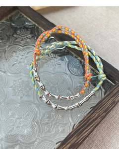 Detail of colorful woven cord bracelets with silver bamboo nodes on vintage glass