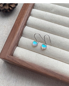 Detalle macro de pendientes de corazón de plata y piedra de luna en caja de joyas