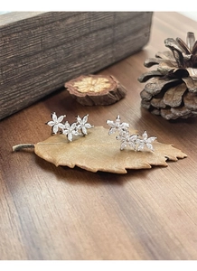 Macro detail of silver triple flower earrings with cubic zirconia on a natural wood leaf