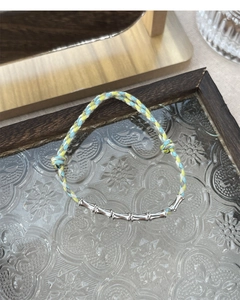 Detail of S925 silver bamboo joints on colorful hand-woven cord bracelet displayed on glass
