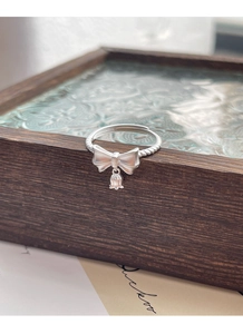 Detail of S925 silver ring featuring a matte bow and small bell pendant on twisted band
