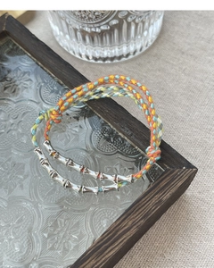Macro detail of S925 silver bamboo charms on colorful hand-woven braided bracelets