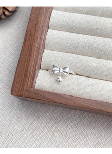 Detailed macro view of S925 silver bow ring with bell pendant on wooden tray