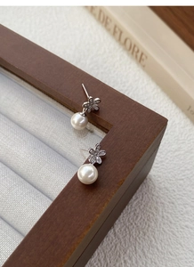 Dettaglio di orecchini a fiore con perle in argento S925 su un cofanetto in legno vintage