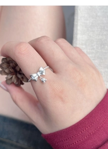 Close-up of S925 silver lily of the valley ring with bow charm on finger