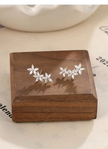 Macro shot of silver five-petal flower earrings with zircons on a wooden block