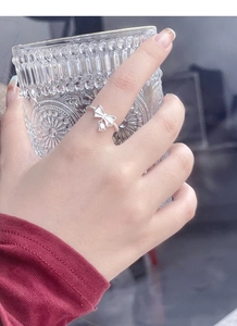 Macro shot of S925 silver bow ring with bell pendant on twisted band and hand model