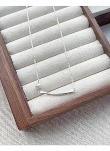 Detail of silver S925 necklace with freedom engraving and a freshwater pearl on wood