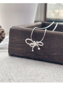 Détail d'un collier avec pendentif nœud en argent 925 posé sur un coffret en bois brun