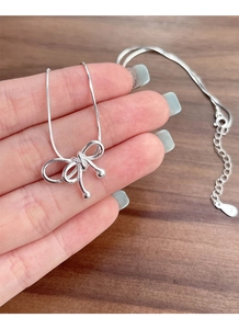 Détail du pendentif nœud en argent S925 avec chaîne serpent sur fond de bois sombre