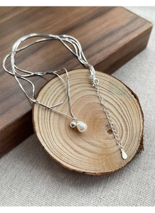 Dettaglio della collana a doppia catena in argento S925 con perla su sfondo in legno