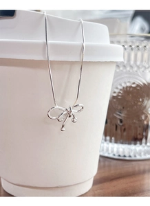 Détail d'un pendentif nœud argenté sur une chaîne serpent posée sur une tasse