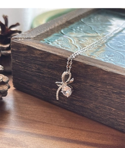 Gros plan du collier pendentif nœud argenté avec zircone étincelante sur boîte en bois