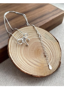 Détail du collier avec pendentif nœud en argent S925 sur une tranche de bois rustique