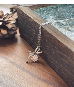 Détail du collier noeud en argent S925 avec diamant posé sur un socle en bois rustique