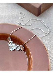 Detail of S925 sterling silver snake chain with irregular metal charms on ceramic plate