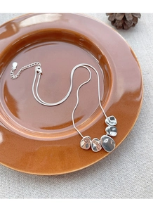 Detail view of silver snake chain with irregular polished pendants on ceramic tray