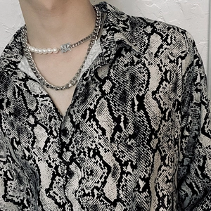 Dettaglio collana a due strati con catena cubana, perle e chiusura con logo C argento