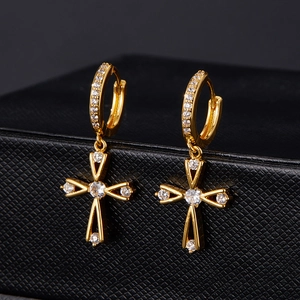 Détail de boucles d'oreilles croix dorées serties de zircons sur fond noir texturé