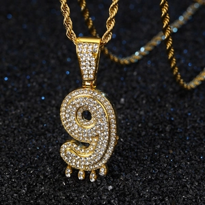 Vue macro d'un pendentif hip-hop chiffre 9 doré avec strass et chaîne torsadée dorée