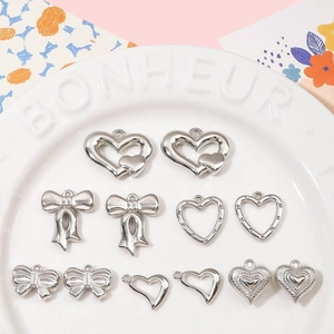 Silver heart and bow DIY pendants displayed on a white ceramic plate for jewelry making