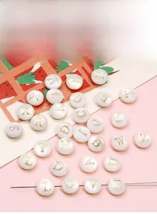 Flat lay of white seashell-style alphabet beads with gold letters for DIY jewelry