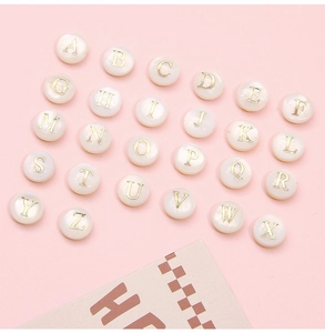 Flat lay of 26 alphabet shell beads with gold letters for DIY jewelry making