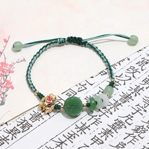 Detailed close-up of a green braided bracelet featuring a golden lion and Fu character bead