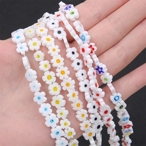 Flat millefiori glass flower beads for DIY jewelry making held in hand over black background