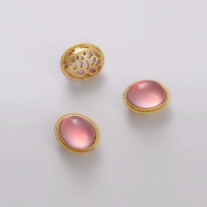 Detalle de tres dijes ovalados dorados con gemas rosas y patrones calados en el dorso