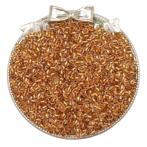 Close-up of amber gold glass seed beads in a tray with a silver bow for DIY jewelry