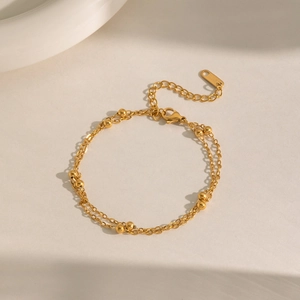 Détail d'un bracelet double couche en acier doré avec perles et fermoir mousqueton