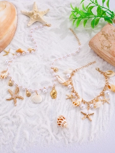 Detail of seashell necklace and bracelet set with pearls on white beach sand background