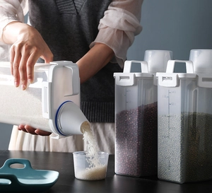 Detail of 2.0L cereal dispenser showing measuring cup lid and grain pouring action
