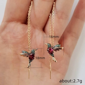 Rose gold hummingbird drop earrings with red and green stones held in hand
