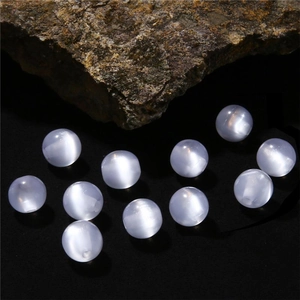 Macro detail of eleven white cat eye resin beads on dark rock for DIY jewelry making