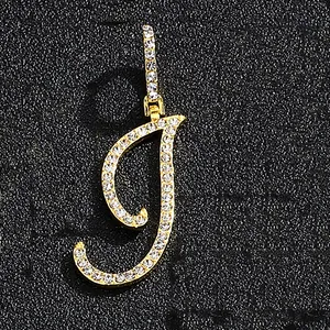 Close-up of golden letter J pendant featuring iced out cubic zirconia on black texture