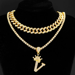 Macro shot of layered gold cuban and tennis chains with iced out crown letter V pendant